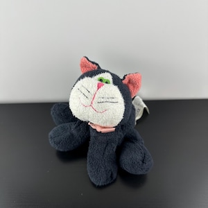 May include: A plush black cat toy with a white face, pink ears, and a pink bow. The cat has green eyes and stitched whiskers. The toy is made of soft material and is designed to be cuddly.