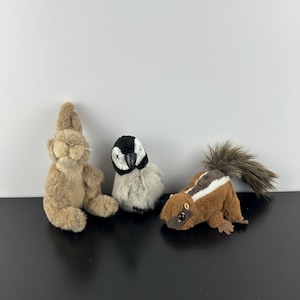 May include: Three plush animal toys: a tan rabbit, a black and white bird, and a brown squirrel with a striped back. The toys are made of soft, textured materials and are designed to resemble real animals.