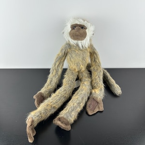May include: A soft toy monkey with long, dangling limbs. The monkey features a brown face and feet, and a white fur ruff. The body and limbs are a mix of brown and tan fur.