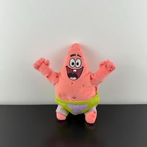 May include: A plush toy of Patrick Star from the animated series Spongebob Squarepants. The pink starfish character has a smiling face, open arms, and is wearing green and purple shorts. The toy is approximately 8 inches tall.