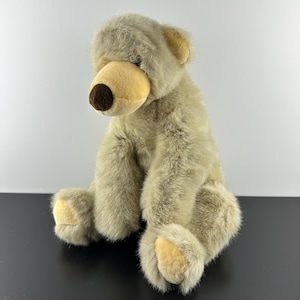 Könnte beinhalten: Ein Plüschbär mit zotteligem, hellbraunem Fell, einer glatten beigen Schnauze, einer dunkelbraunen Nase und beigen Pfotenpolstern. Das Stofftier sitzt in einer aufrechten Position und besteht aus weichem, strukturiertem Stoff mit runden Ohren.