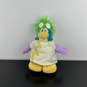 May include: A plush penguin toy with green hair, goggles, and a yellow beak. The penguin wears a white lab coat with a yellow lightning bolt design and purple gloves. The penguin has yellow feet.