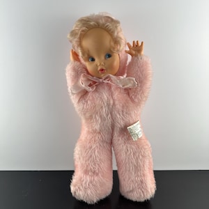 May include: A vintage pink plush doll with blonde hair and blue eyes. The doll is wearing a pink fuzzy jumpsuit with a pink bow.