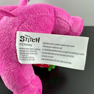 Op de afbeelding: Een close-up van een roze pluche speelgoed met een label met de tekst "Disney Stitch". Het label bevat ook wasvoorschriften en materiaalinformatie. Het pluche speelgoed is gemaakt van polyestervezels.