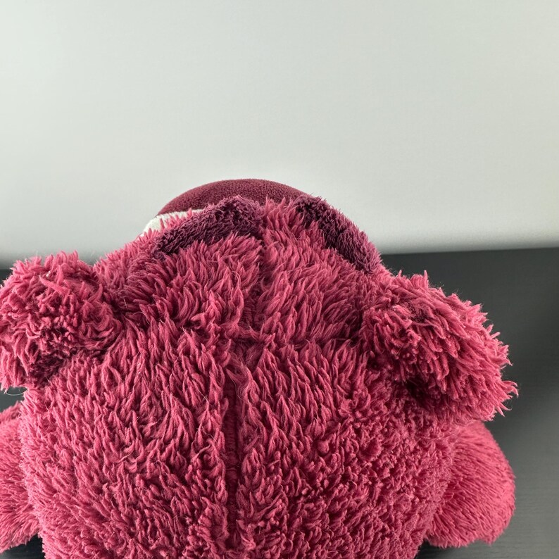 May include: A plush, pink teddy bear with a textured, fuzzy exterior. The bear has a darker pink head and ears, with a lighter pink muzzle. The toy is soft and cuddly, perfect for children or collectors.