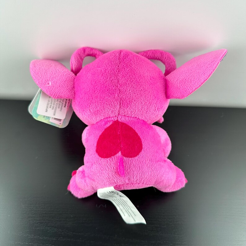Op de afbeelding: Een felroze pluche speelgoed met grote oren, een hartvormig ontwerp op de rug en een kleine staart. Het speelgoed heeft een label bevestigd. Het pluche is gemaakt van zacht materiaal.
