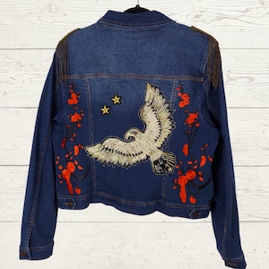 May include: A blue denim jacket with embroidered red flowers and a white eagle on the back. There are two gold stars above the eagle.