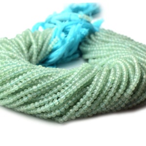 May include: A large strand of light green gemstone beads. The beads are round and have a slightly frosted finish. The strand is coiled into a circle.
