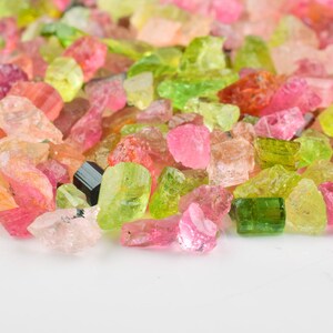 Hand-held raw tourmaline stones showing color variations and natural formation.