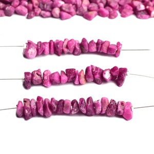 Può includere: Tre fili di perline di pietre preziose rosa infilate su un filo d'argento. Le perline sono di forma irregolare e hanno una texture ruvida e naturale.