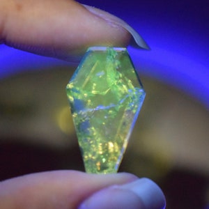 May include: A green, faceted, crystal-like object with a pointed tip. The object is held in a hand and appears to be made of glass.