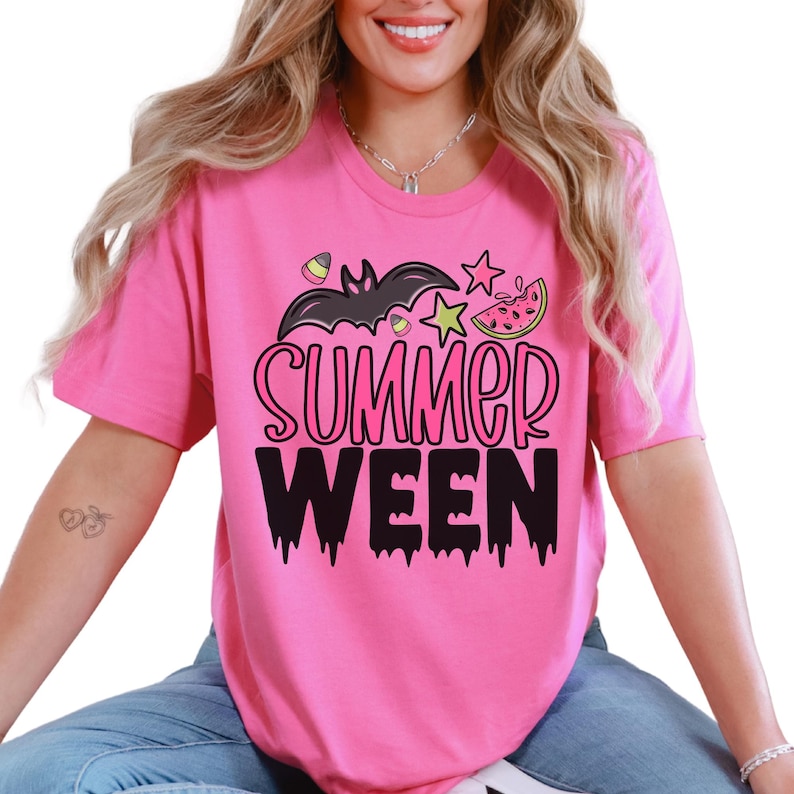 May include: A pink t-shirt with the words "SUMMER WEEN" in black, with a bat, stars, and watermelon graphic. The shirt has short sleeves and a round neckline.