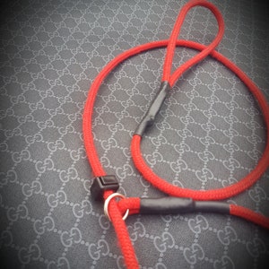 May include: A red rope dog leash with a black and silver clasp. The leash is on a black and white patterned surface.