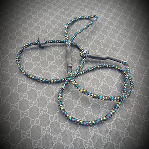 May include: A black rope leash with colorful accents, featuring a black clip. The leash is coiled on a patterned surface.