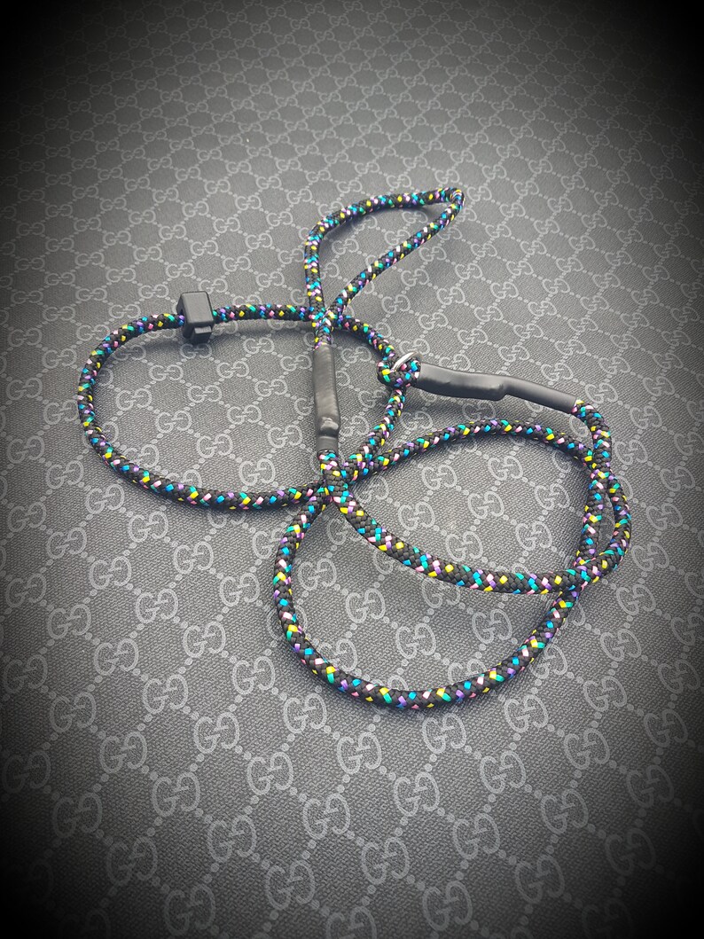 May include: A black rope leash with colorful accents, featuring a black clip. The leash is coiled on a patterned surface.