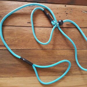 May include: A turquoise blue rope dog leash with black accents and a metal ring. The leash is coiled on a wooden surface.