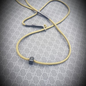 May include: A yellow rope dog leash with black accents and a silver ring. The leash is lying on a gray and white patterned surface.
