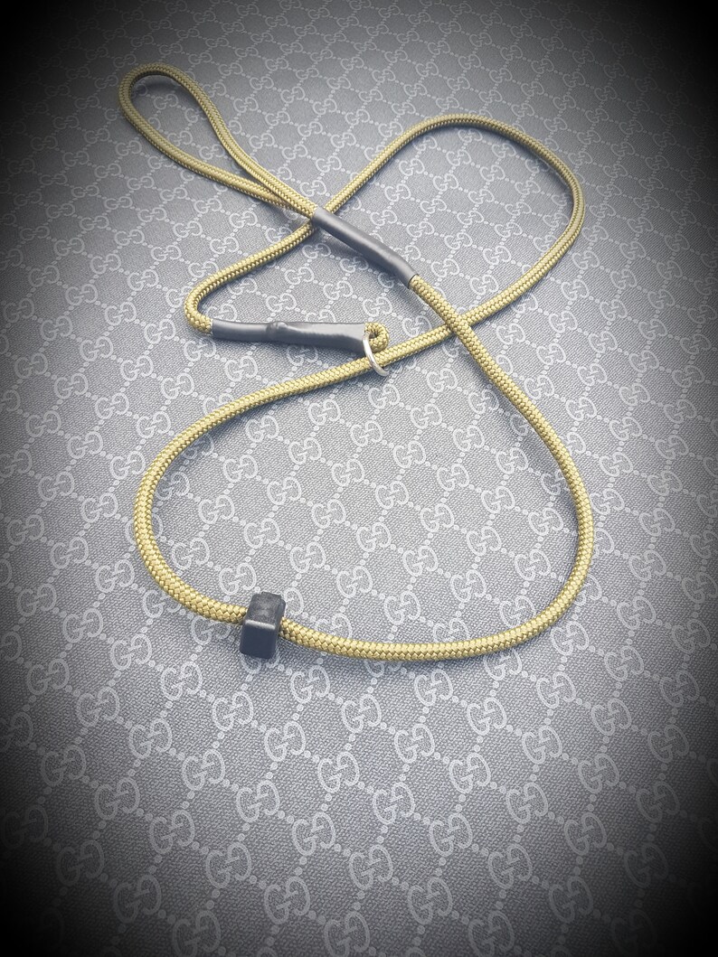 May include: A yellow rope dog leash with black accents and a silver ring. The leash is lying on a gray and white patterned surface.