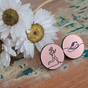 May include: Two pink wooden round pins with black line drawings. One pin features a runner and the other pin features a person on a snowboard.