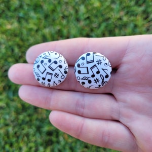 May include: A pair of white button earrings with a black musical note pattern.
