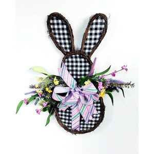 May include: A black and white checkered bunny wreath with a pink and green striped bow and a bouquet of purple, yellow, and green flowers.