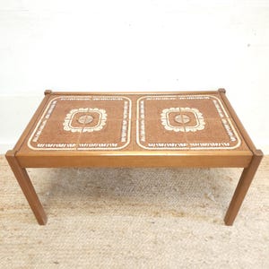 May include: A mid-century modern coffee table with a tiled top. The tiles are brown with a white geometric pattern. The table has a simple wooden frame.