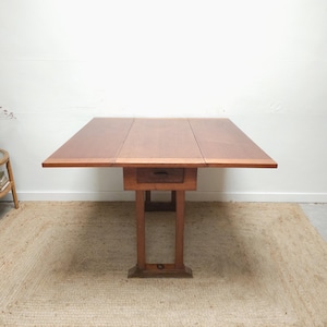May include: A wooden drop-leaf table with a rectangular top and a single drawer. The table is a warm brown colour and has a sturdy, rectangular base. The table is approximately 152 cm long when fully extended.