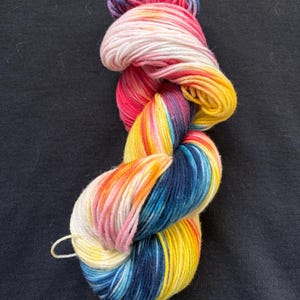 May include: A vibrant skein of yarn, featuring a gradient of colours such as pink, yellow, blue, and purple. The yarn is tightly wound, suitable for knitting or crochet projects. The yarn displays a mix of bright and pastel shades.