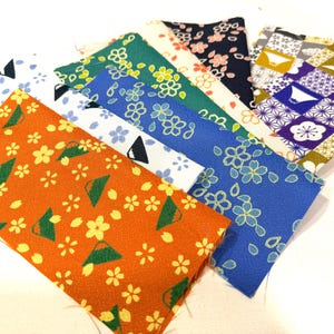 May include: A collection of colorful fabric swatches with Japanese-inspired patterns. The swatches feature floral and geometric designs in various colors, including orange, blue, green, and purple. The fabric is likely cotton or a similar material.
