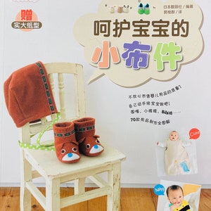 May include: A book cover with a light brown background and a speech bubble with the text "呵护宝宝的小布件" in black. The book cover features a white chair with a brown hat and a pair of brown shoes with blue eyes and a brown nose on the seat. The book cover also features a photo of a baby wearing a white onesie with a yellow bee design and the text "happy" in a red circle.