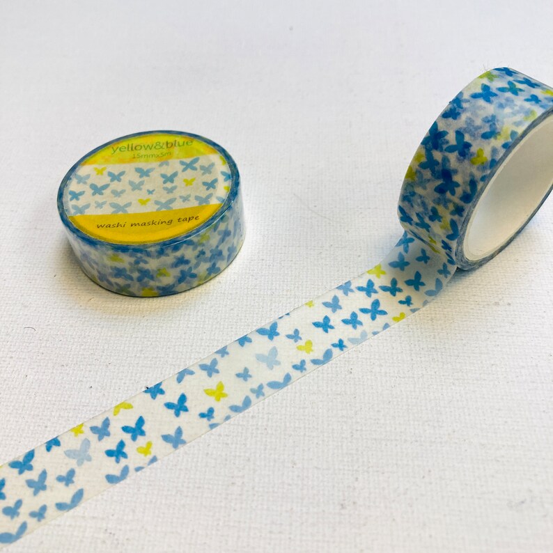 May include: A roll of blue and yellow washi tape with a butterfly pattern. The tape is labelled "yellow&blue 15mm washi masking tape".