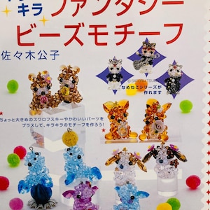 Pode incluir: Uma capa de revista com figuras de animais de contas. O título japonês traduz-se por "Motivos de contas de fantasia". As figuras são feitas de cristais Swarovski e vêm em cores como ouro, azul e roxo. A revista também apresenta texto em japonês.