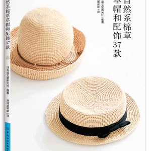May include: A book titled "Natural Cotton Straw Hats and Accessories 33 Designs" with two straw hats on the cover. The top hat is a light brown fedora with a brown ribbon. The bottom hat is a light brown fedora with a black ribbon tied in a bow.