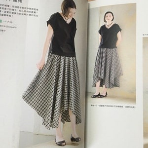 May include: A woman wearing a black V-neck top and a black and white plaid skirt. The skirt has an asymmetrical hemline. The image is from a fashion magazine.