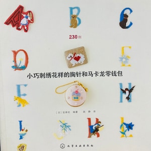 May include: A book cover with the title "Brooch & Macaron Pouch" in white text on a blue background. The book cover features colorful embroidered designs of letters, animals, and other motifs. The text "230例" is also visible on the cover. The book cover is in Japanese.
