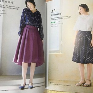 May include: Two women modeling outfits from a fashion magazine. One wears a dark blue floral blouse and a pleated purple skirt. The other wears a white top and a navy skirt with white polka dots. The magazine pages are open.