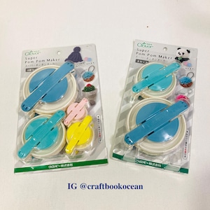 Puede incluir: Dos juegos de Super Pom-Pom Maker Clover en embalaje transparente. Cada juego incluye cuatro pompones en azul, turquesa, rosa y amarillo. El embalaje presenta texto japonés e ilustraciones de pompones. El identificador de Instagram @craftbookocean es visible.