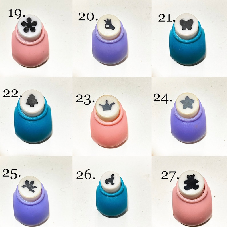 May include: A collection of nine craft paper punches labeled 19 through 27, featuring various shapes including a flower, hand gesture, butterfly, tree, crown, star, angel, seal, and bear, set in pink, purple, and blue plastic housings.