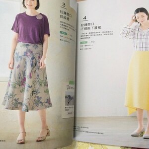 May include: Two women modeling clothing from a fashion magazine. One wears a purple t-shirt and floral skirt. The other wears a plaid shirt and yellow skirt. The magazine pages are open, displaying text and illustrations.