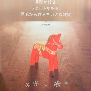Könnte beinhalten: Eine rote Dala-Pferd-Figur aus Filz mit weißen und gelben Akzenten steht auf einer Holzoberfläche. Das Bild enthält japanischen Text und Schneeflockenmuster. Die Figur ist ein traditionelles skandinavisches Volkskunstobjekt.