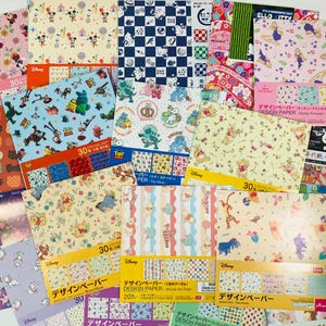 Puede incluir: Una colección de blocs de papel de diseño con temática de Disney y Sanrio que presentan varios estampados de personajes, incluidos Mickey Mouse, Toy Story, Winnie the Pooh, Hello Kitty y princesas de Disney, con 30 hojas por bloc.