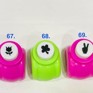 May include: Five colorful craft paper punches arranged in a row, labeled 66 through 70. The punches are purple, pink, lime green, hot pink, and purple. Each white top button features a black icon: a fish skeleton, tulip, clover, peace sign, and 'I love you'.