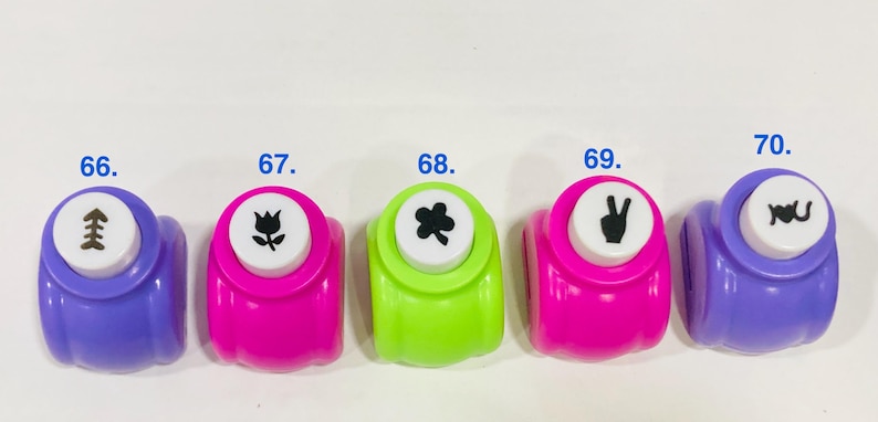 May include: Five colorful craft paper punches arranged in a row, labeled 66 through 70. The punches are purple, pink, lime green, hot pink, and purple. Each white top button features a black icon: a fish skeleton, tulip, clover, peace sign, and 'I love you'.