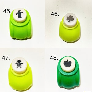 May include: Four green paper punches labeled 45 through 48. Number 45 features a penguin, 46 a clover, 47 a person, and 48 an apple. Each punch has a white circular top with a black icon representing the shape it cuts, set in a green plastic body.