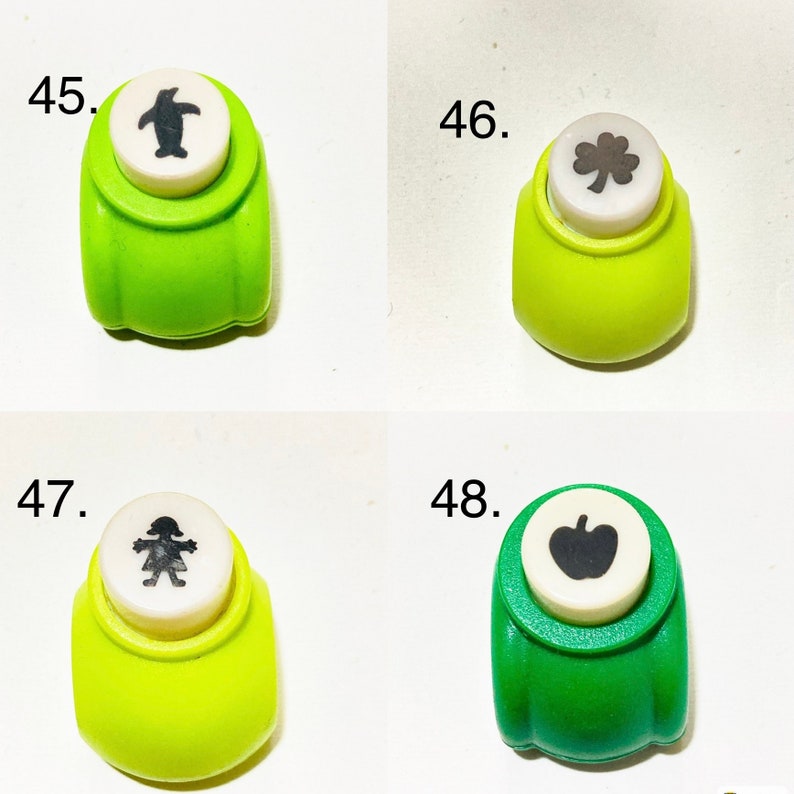 May include: Four green paper punches labeled 45 through 48. Number 45 features a penguin, 46 a clover, 47 a person, and 48 an apple. Each punch has a white circular top with a black icon representing the shape it cuts, set in a green plastic body.