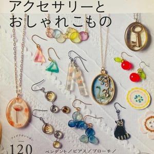 Puede incluir: Una colección de accesorios hechos a mano con resina UV, que incluyen collares, pendientes y broches. La imagen muestra varios diseños, como un colgante de llave, pendientes de cereza y un pendiente con forma de gato. El texto de la imagen dice "accesorios de resina UV".