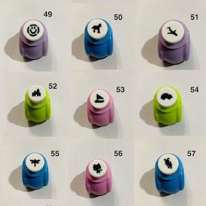 May include: A collection of nine colorful craft paper punches labeled 49 through 57. Each punch features a unique black icon on a white circular top, including a smiley face, horse, airplane, castle, sailboat, car, dragonfly, cat, and rabbit.