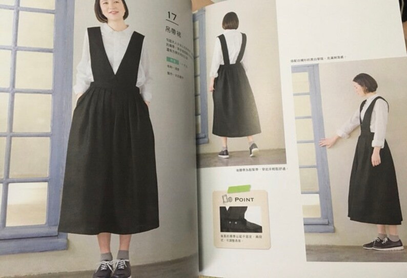 May include: A black overall dress with a deep V-neck, paired with a white blouse. The dress has a full skirt and pockets. The image is from a fashion magazine.
