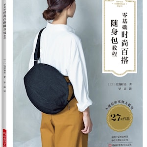 May include: A book cover with a woman wearing a white shirt and brown pants. The book is titled "Zero-Based Fashionable Everyday Bags" and features 27 different bag designs. The book cover is in Japanese.