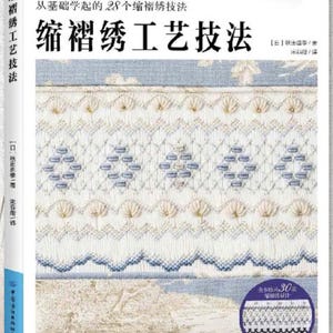 May include: A book cover with a white background and the title "縮褶绣工艺技法" in black text. The book cover features a close-up of a white fabric with blue and white embroidery. The book cover also includes a small image of a fabric sample with a similar embroidery design.